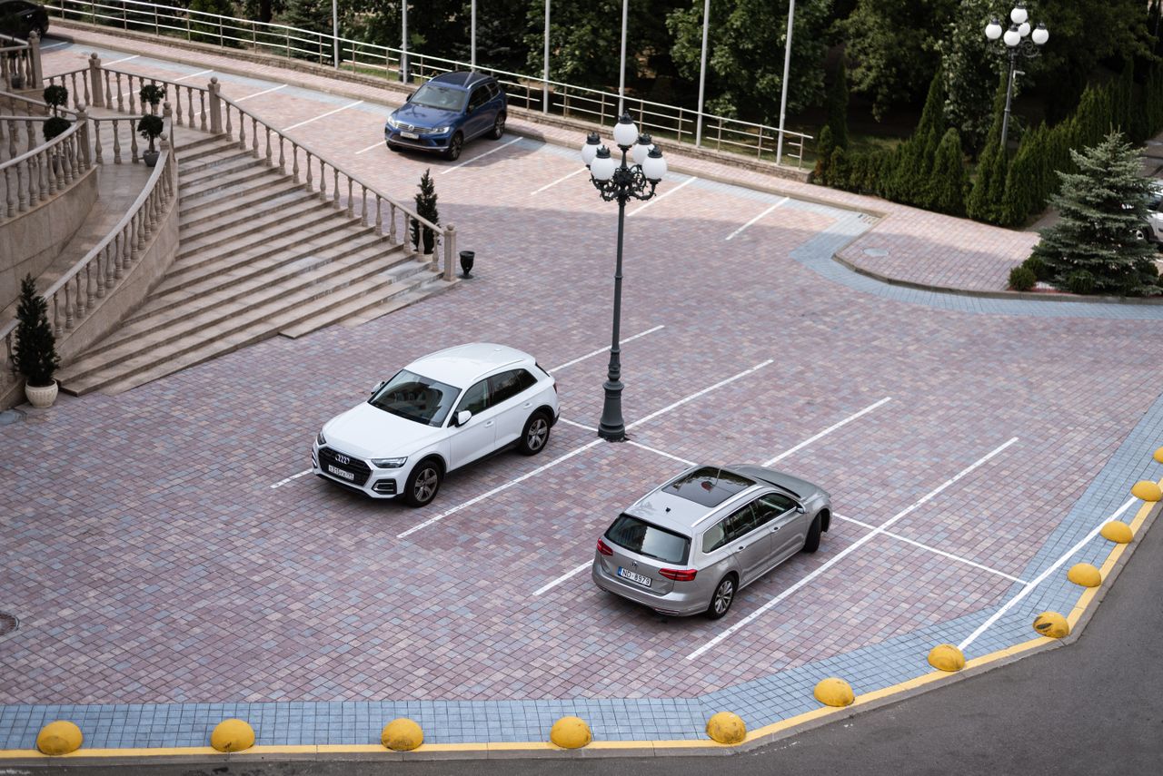 Two cars parked in an elegant outdoor parking lot with surrounding trees.