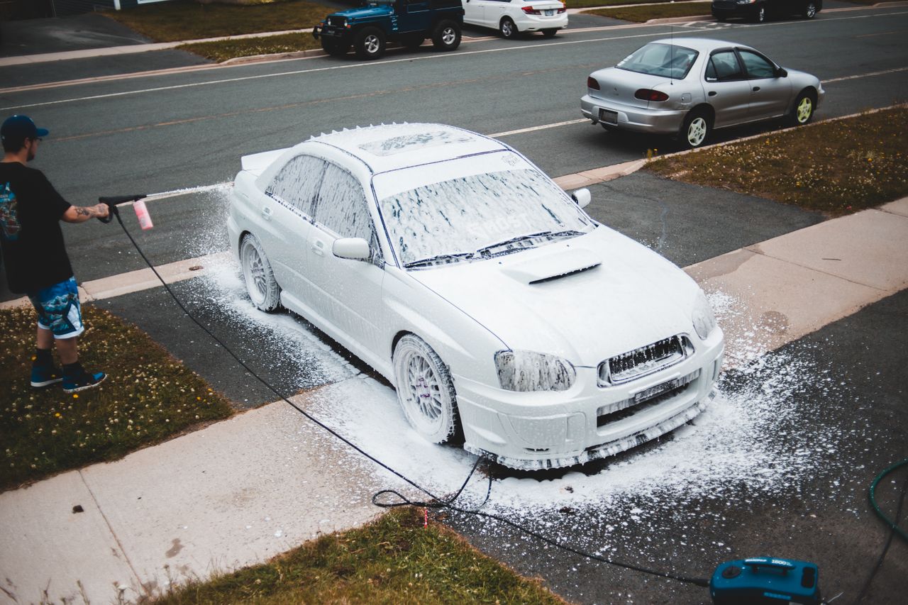 Home From above car covered in foam washing by man in casual wear with pressure washer gun in hand